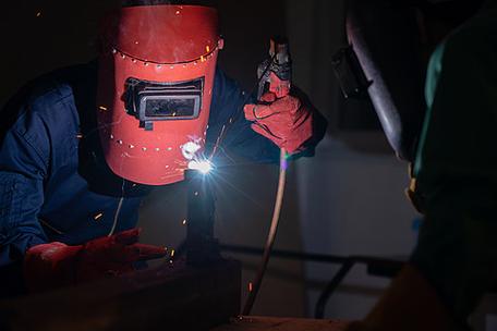 和建筑维护服务金属焊工使用电弧焊机在工厂焊接钢,同时佩戴安全设备.